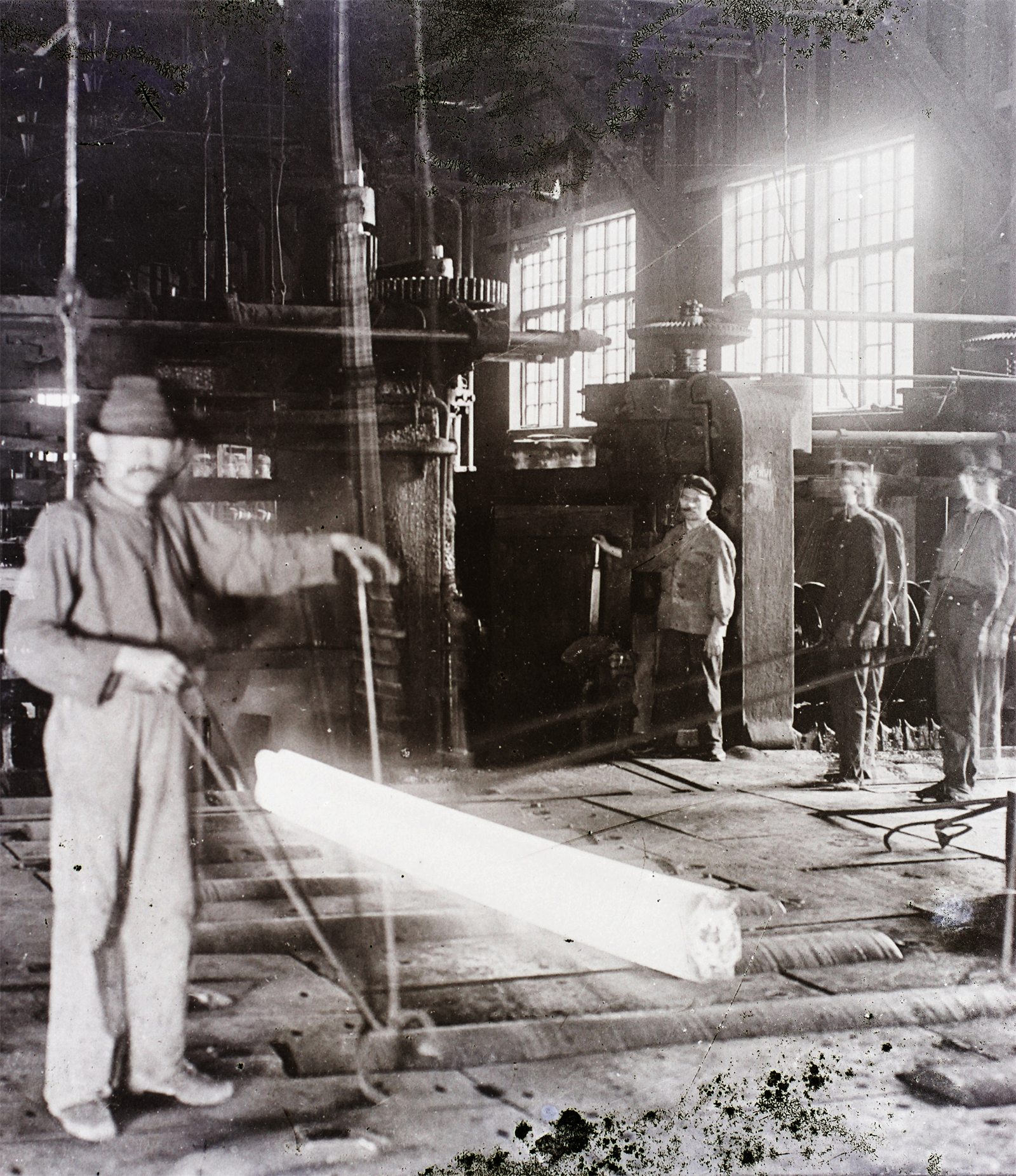 Historic photograph from 1909: a worker guides a glowing steel bar in the rolling mill of the Diósgyőr ironworks